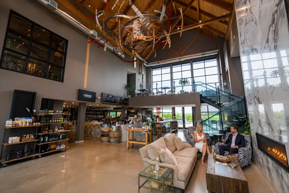 The double-height lounge at Adamo Estate, with a sculptural chandelier, a linear fireplace set into marble, armchairs and the retail shelves beyond.