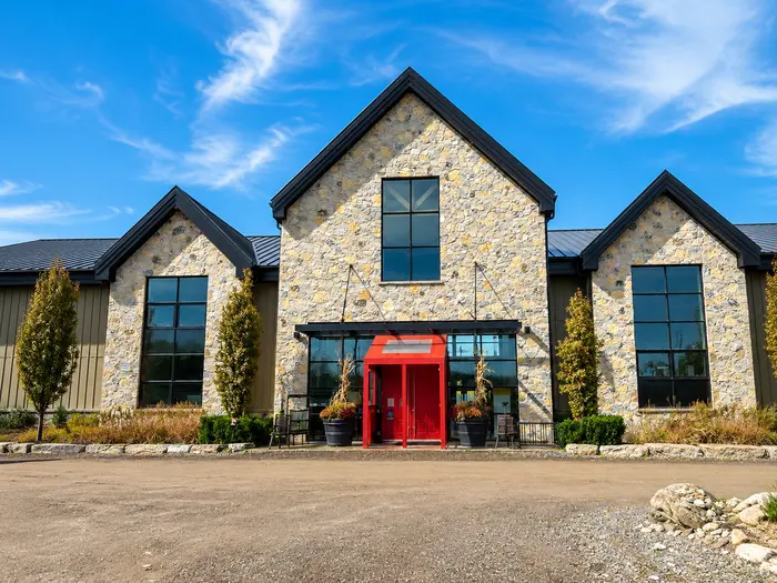 The stone-and-timber winery building at Adamo Estate, with its steep gables and bright red front doors, under a clear autumn sky.