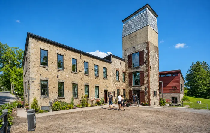 The restored 1880s stone mill at Alton Mill Arts Centre, with its shuttered tower and visitors walking toward the entrance.