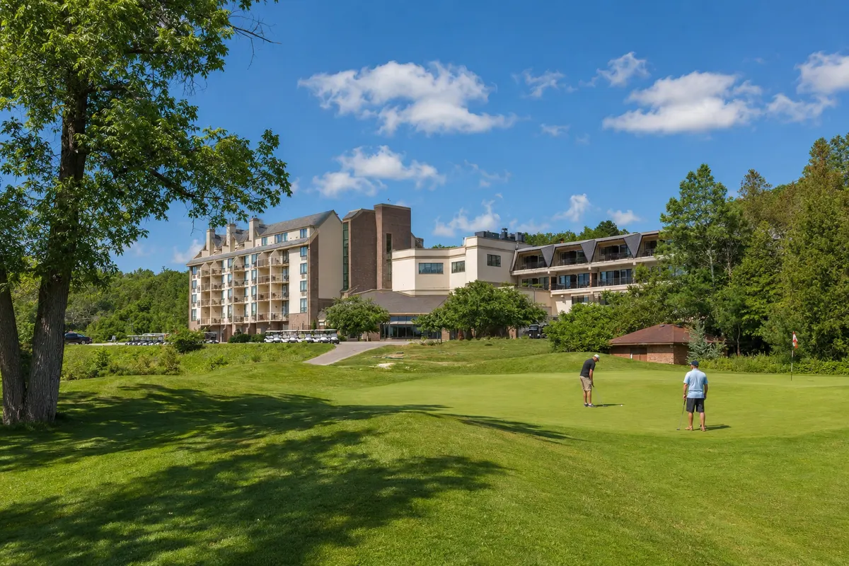 Two golfers putting on a green in front of Hockley Valley Resort on a clear summer day.