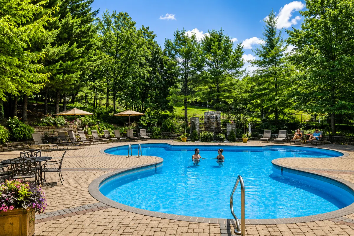 The resort's outdoor pool surrounded by stone paving, loungers and pines, with people swimming on a summer afternoon.