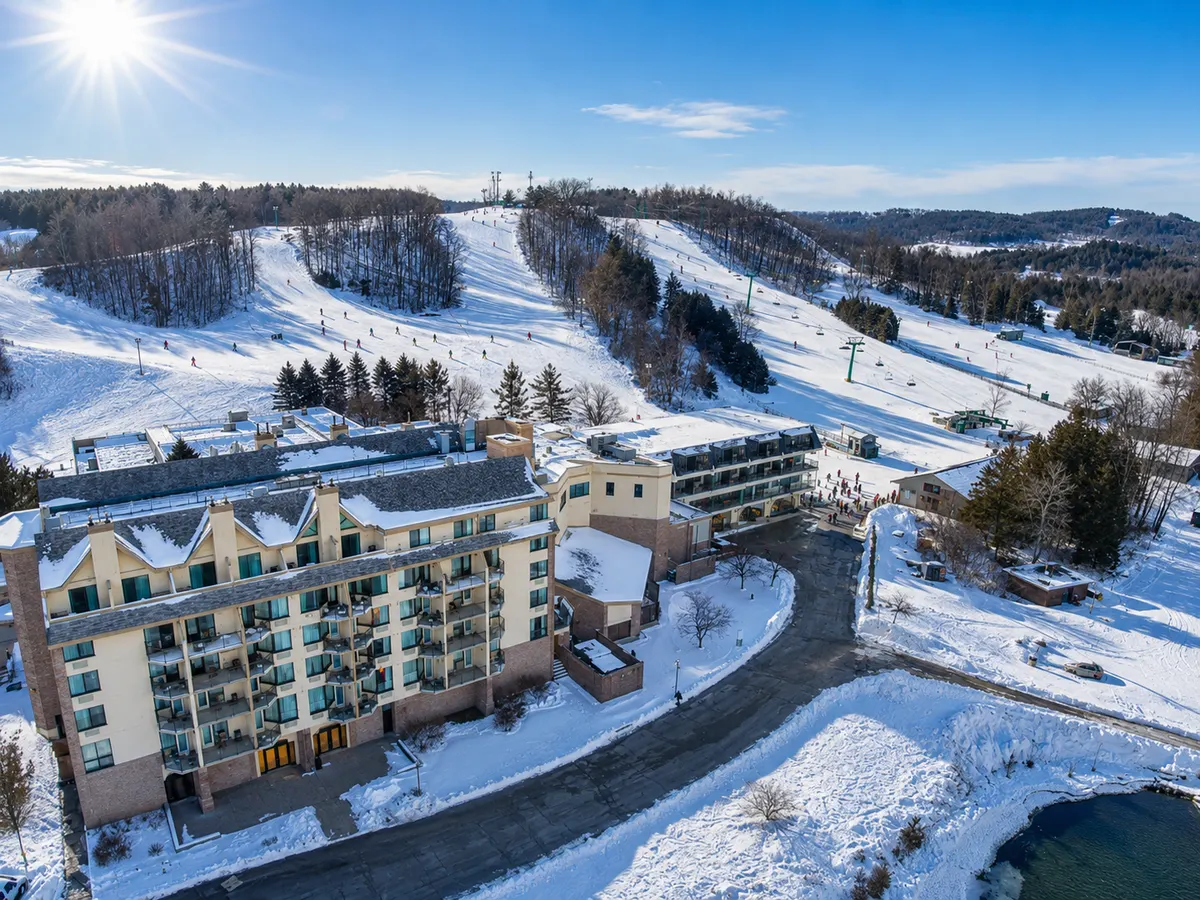 Aerial view of Hockley Valley Resort in winter, with skiers on the groomed runs above the hotel and a chairlift running up the hill.