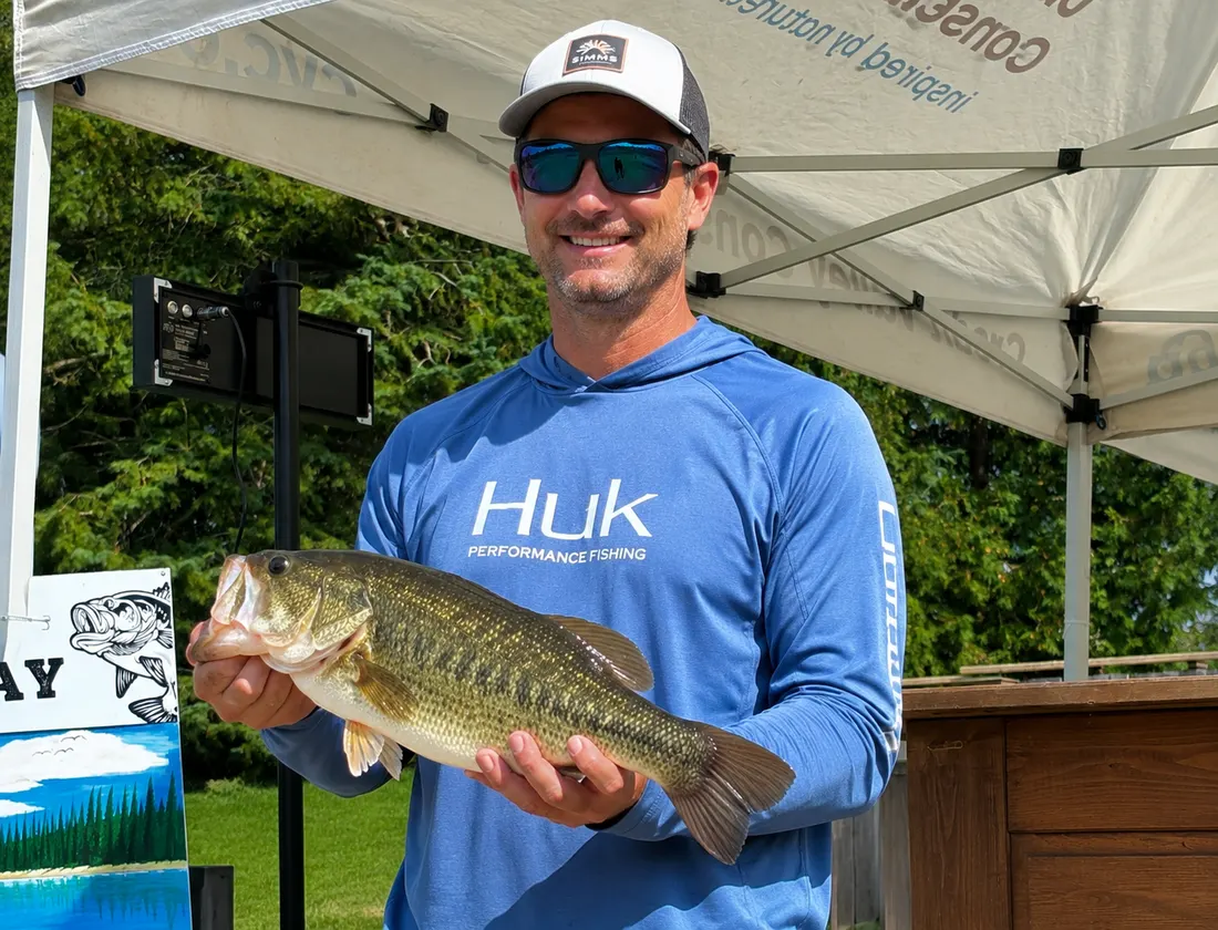 A smiling angler holding a largemouth bass under the Credit Valley Conservation tent at the Island Lake Bass Derby.