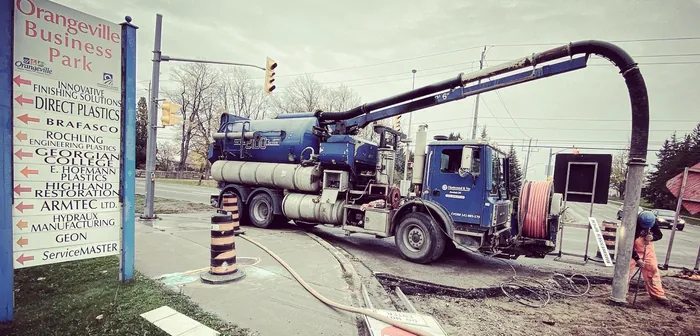 A CT Horizontal & Vac hydrovac truck at the Orangeville Business Park entrance, boom arm extended over an open excavation.