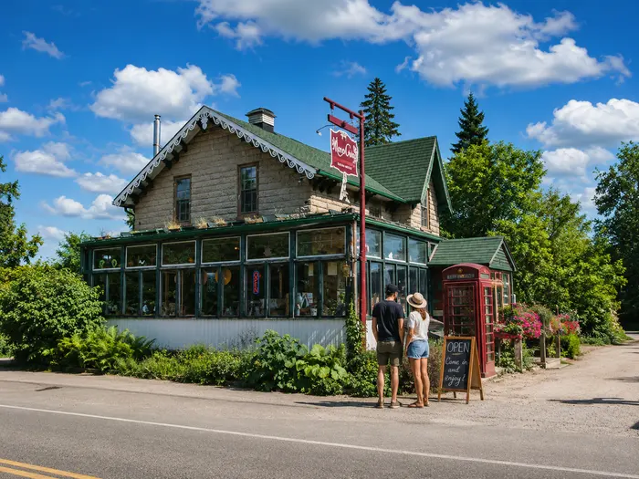 The stone Mono Cliffs Inn on Mono Centre Road, with green trim, a glassed-in conservatory, a red telephone box outside and a chalkboard reading Open, come in and enjoy.