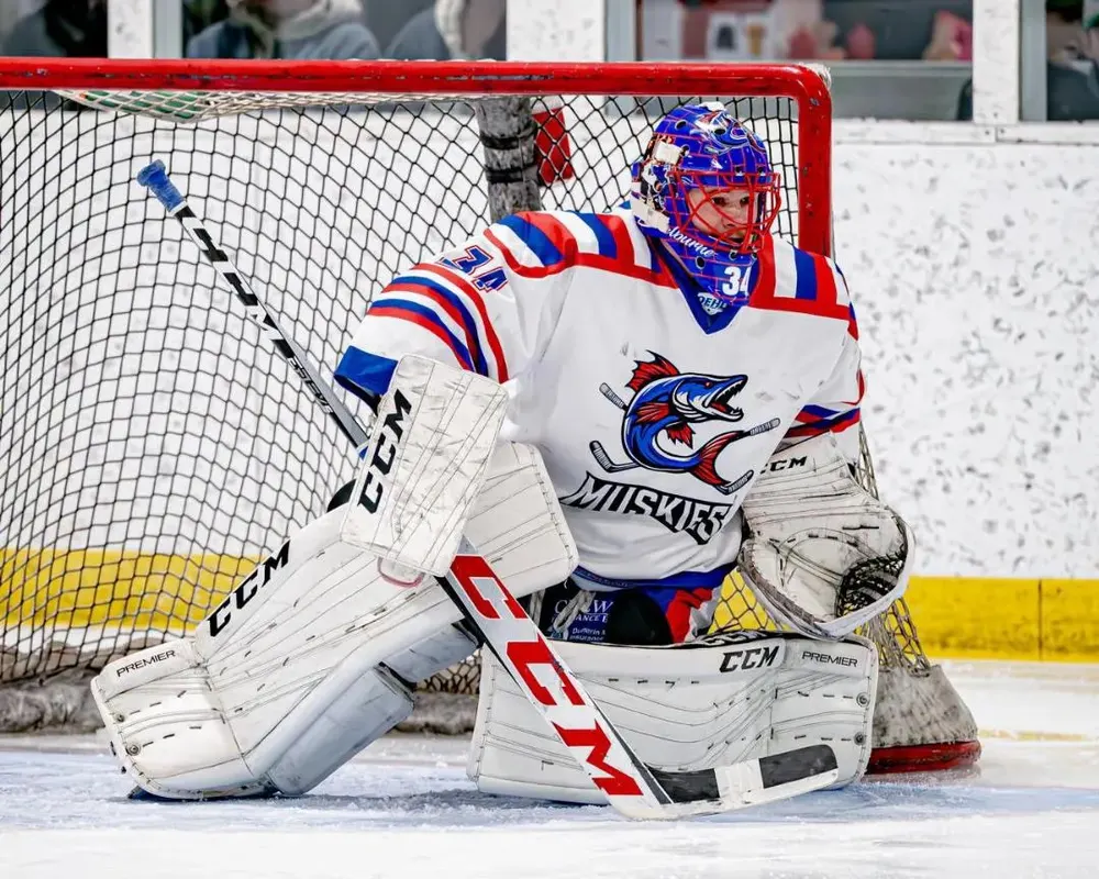 Close-up of the Shelburne Muskies goaltender in the crease, wearing the muskie crest and a red, white and blue mask.