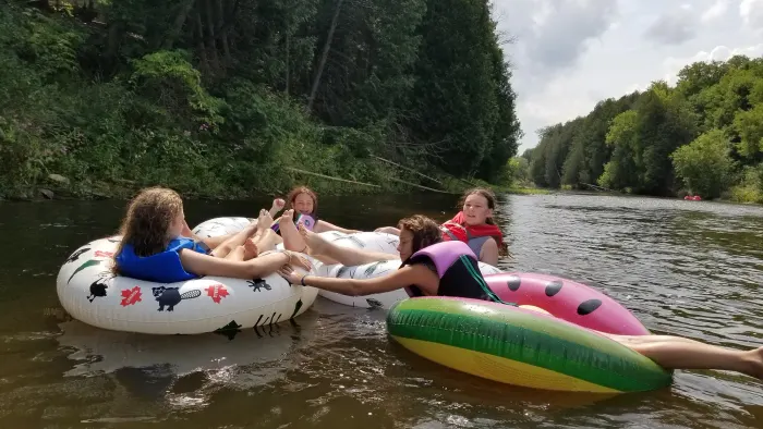 A dozen people floating on inflatable tubes down a wide, calm stretch of the Grand River, with dense green forest along the far bank.