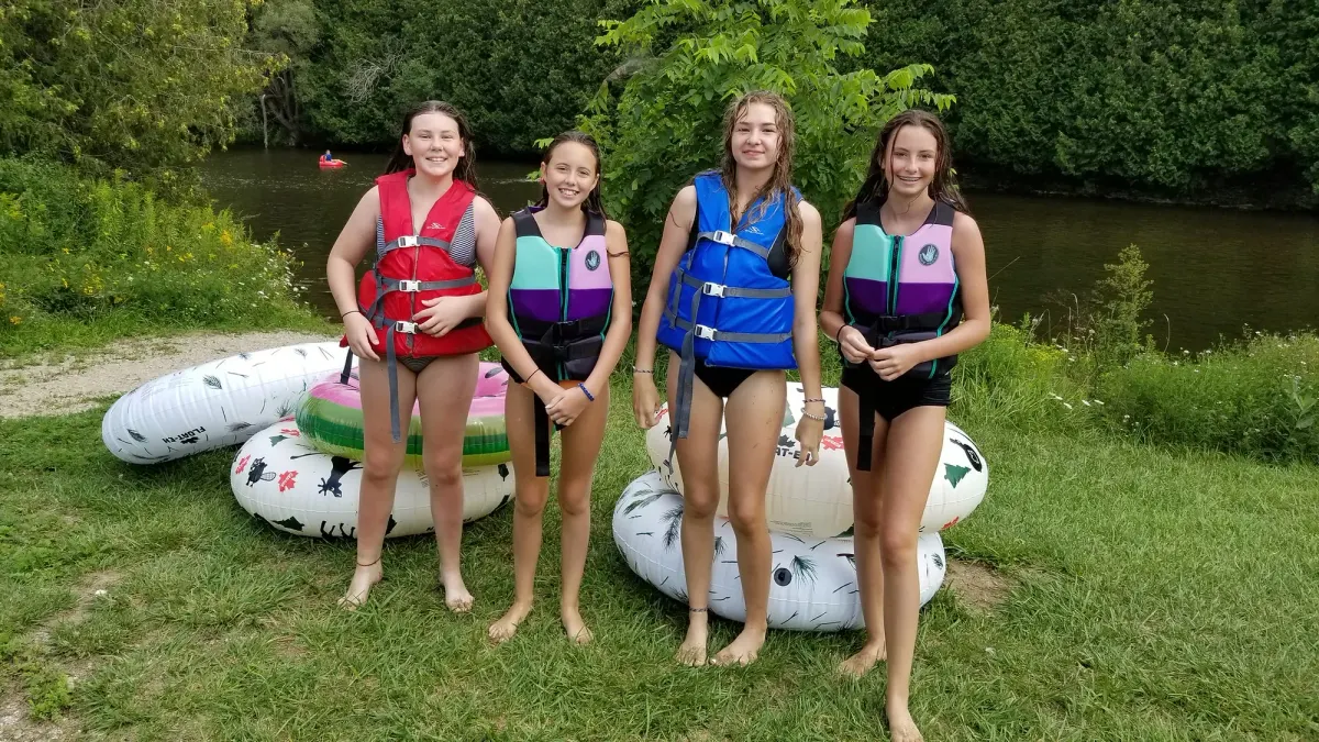 Four young people in life jackets standing on the riverbank beside their river tubes, ready to launch onto the Grand River.